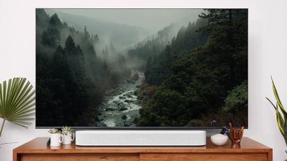 Sonos Beam 2nd Gen on wooden table with TV behind it