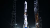 a white rocket stands on a launch pad at night