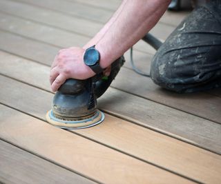 Man sanding wooden decking with an electric sander
