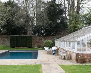 Greenhouse inspired pool house ideas with a traditional garden room and pool in a paved garden with lawns.
