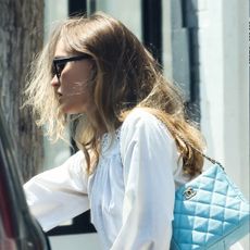 Lily-Rose Depp wearing a white cotton minidress with a teal Chanel shoulder bag and tan ballet pumps.