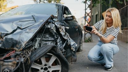 A woman photographs the damage to her car after an accident.