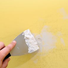 Filling a hole in a yellow wall with filler and a filling knife