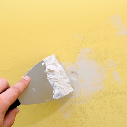 Filling a hole in a yellow wall with filler and a filling knife