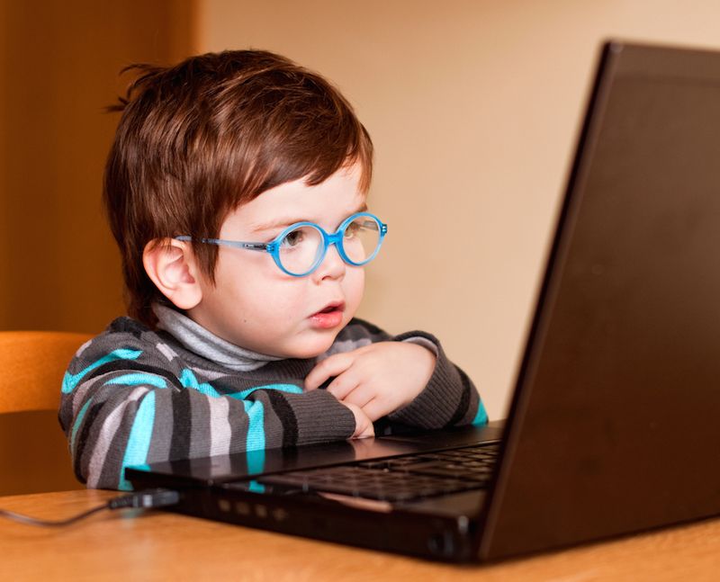 A young boy looks at a computer, wearing glasses