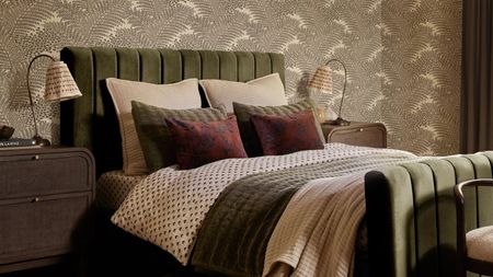 cozy bedroom with pleated lampshades on the nightstands, green velvet bed, and patterned wallpaper