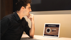 A man with dark hair and a black shirt sits looking approvingly at a Samsung Color E-Paper device showing a coffee advert