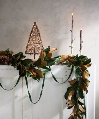 faux Christmas leave garland on shelf with small decorative Christmas tree and long candles