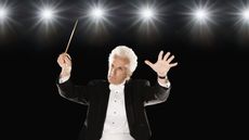 A man wearing a tuxedo conducts an unseen orchestra.