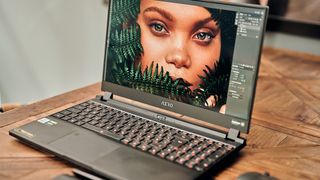 The Gigabyte AERO 15 OLED running image editing software while sitting on a wooden table