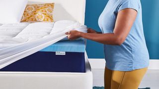 A person fitting the Sleep Innovations Dual Layer Topper on a bed