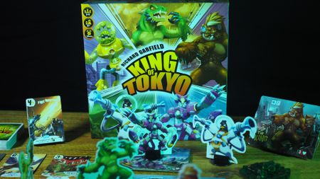 King of Tokyo components, box, and cards on a wooden table against a black background