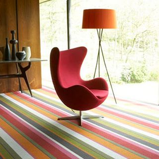 room with stripe carpet and red chair with orange stand lamp