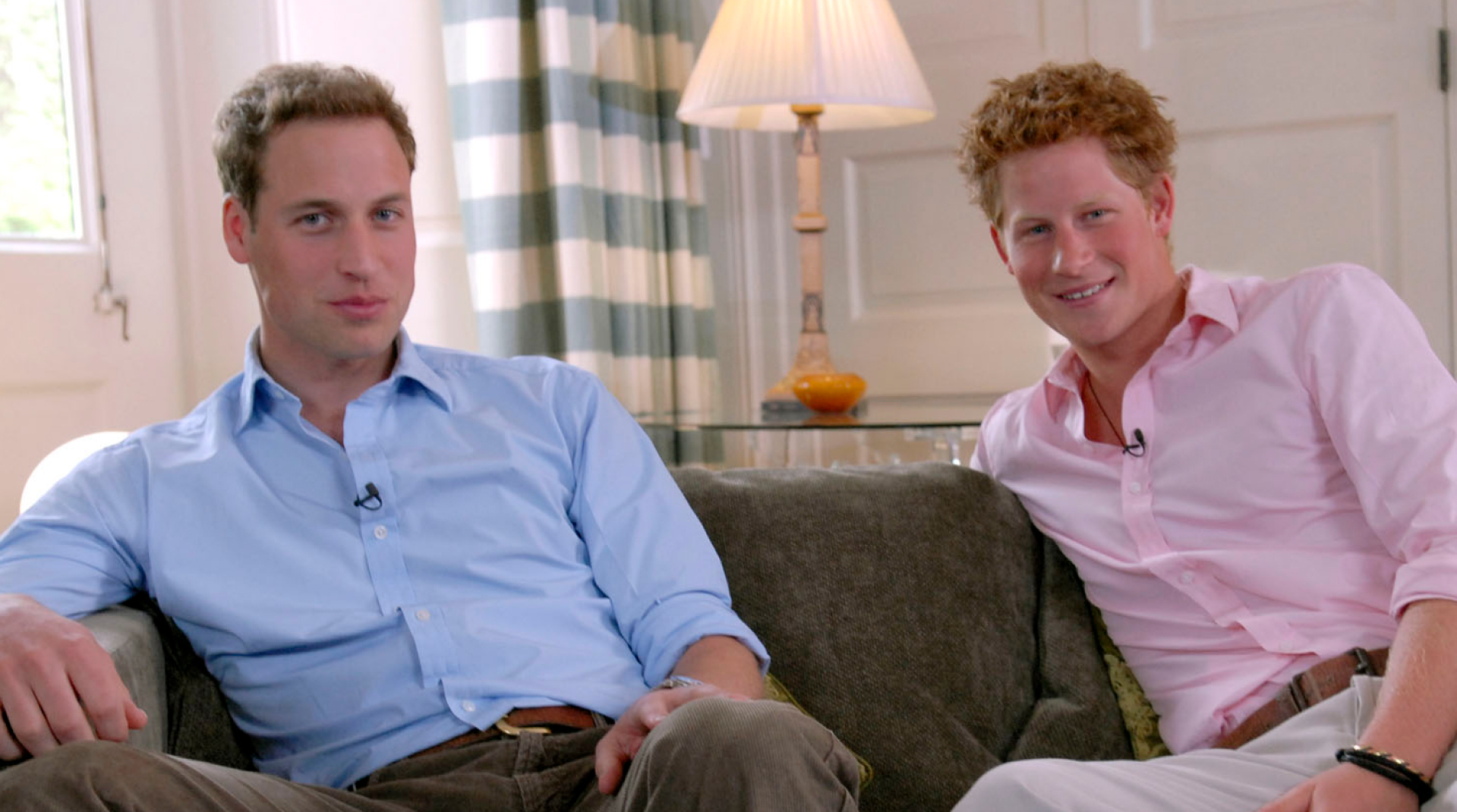 Princes William and Harry pose together on a couch wearing shirts and slacks
