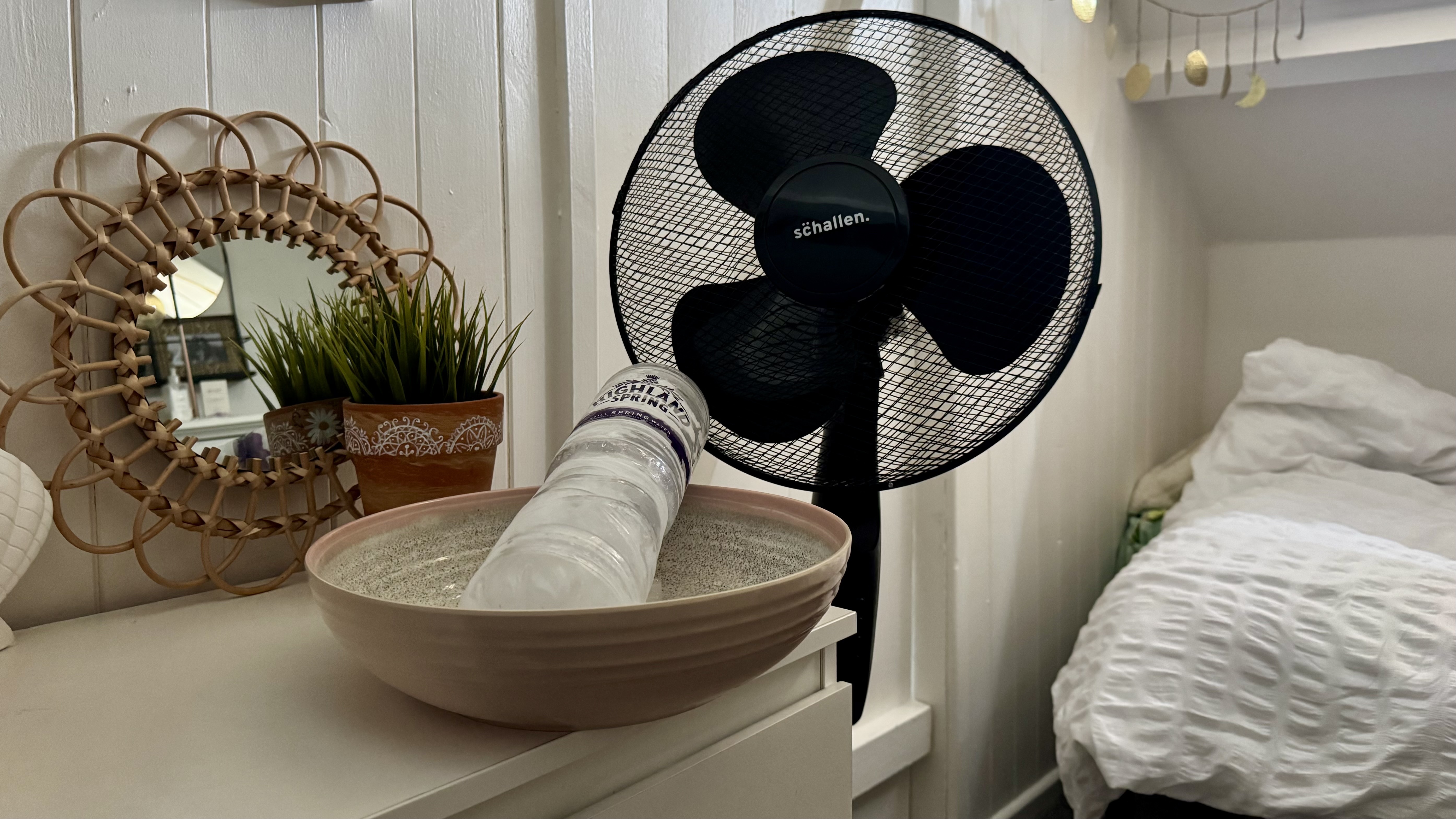 A black fan next to bowl holding a bottle of ice representing DIY air con hack