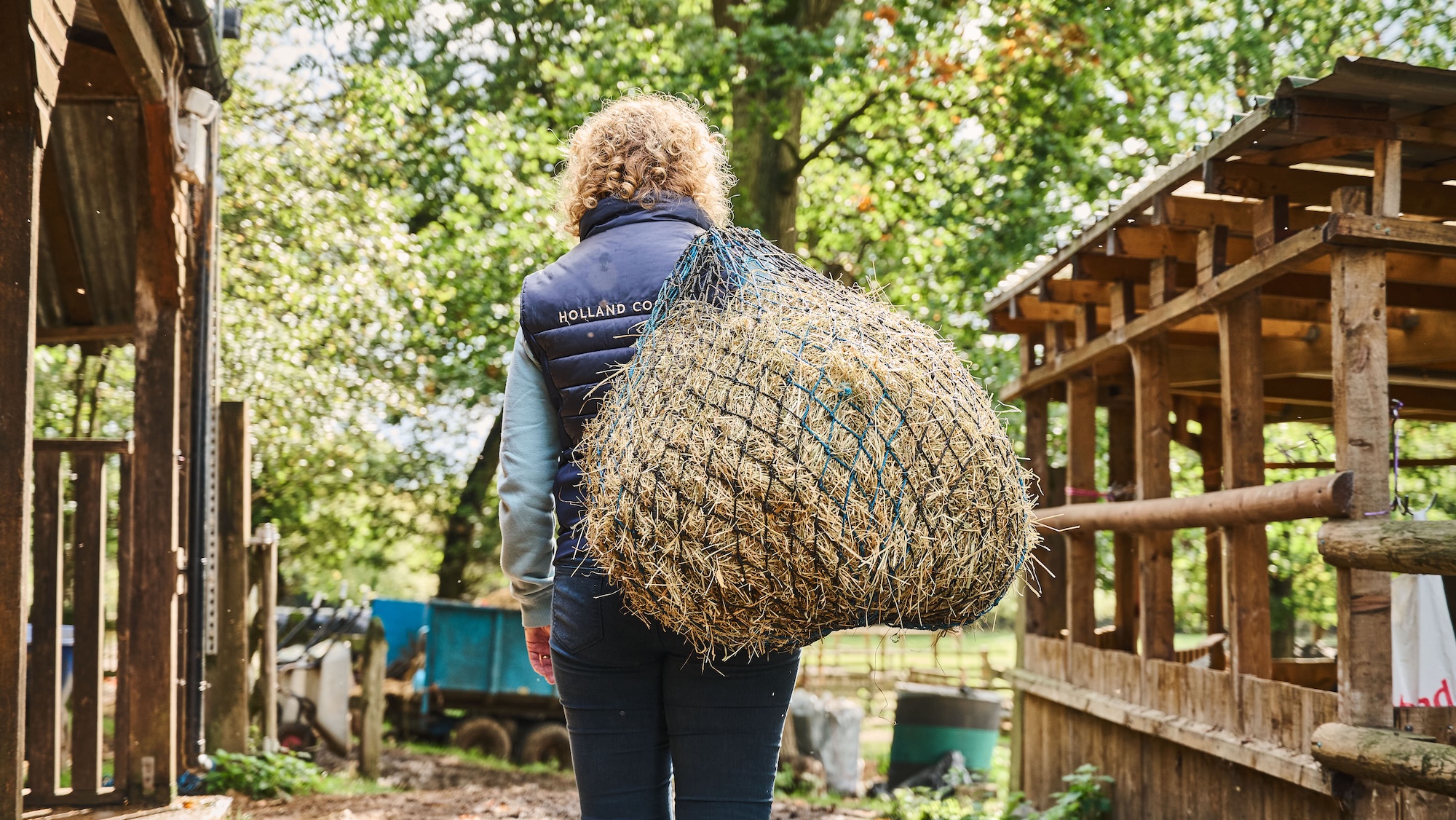 A groom carrying a haynet over her shoulder