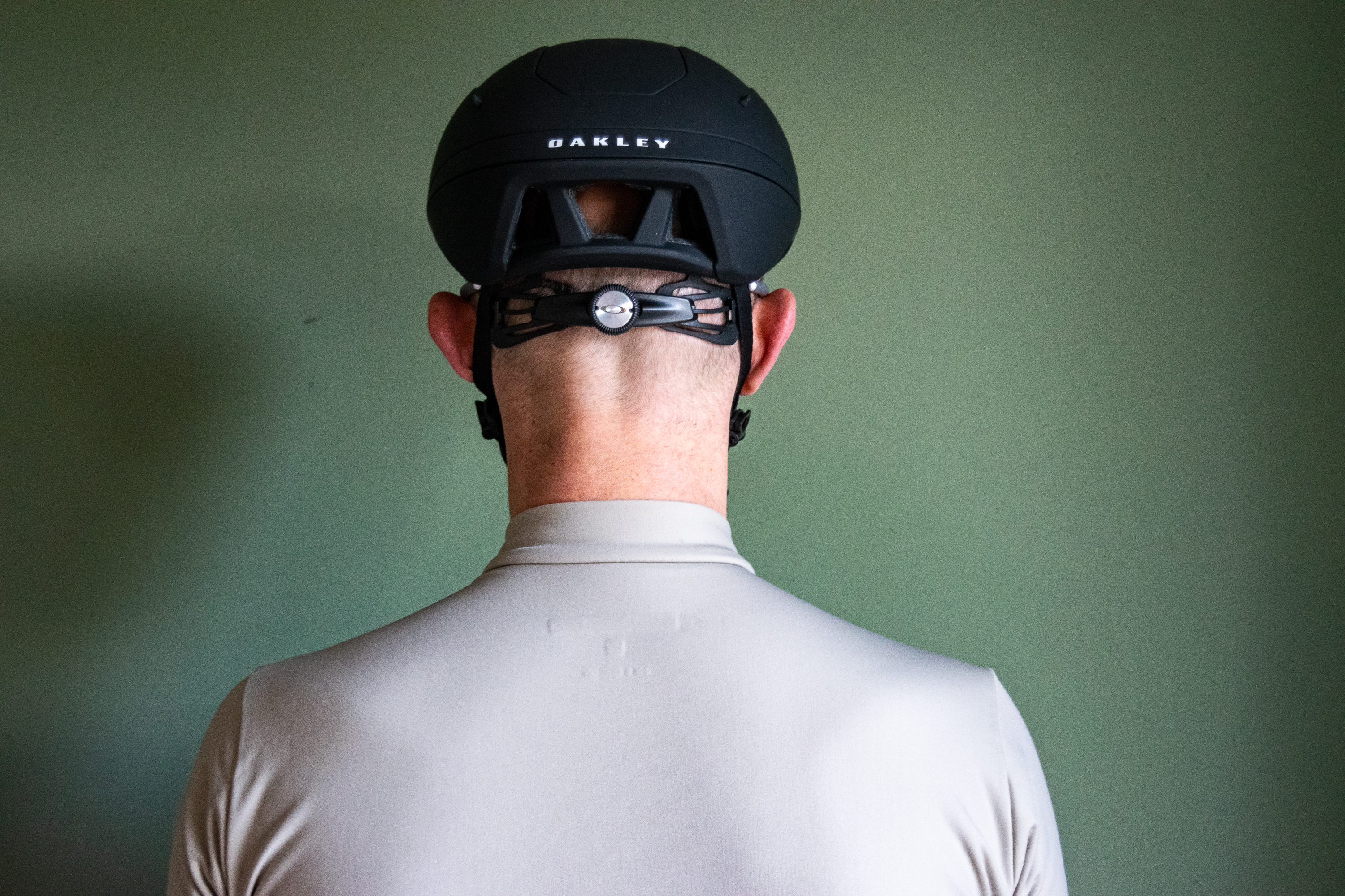 A rider wearing a black Oakley Velo Mac helmet in front of a green wall