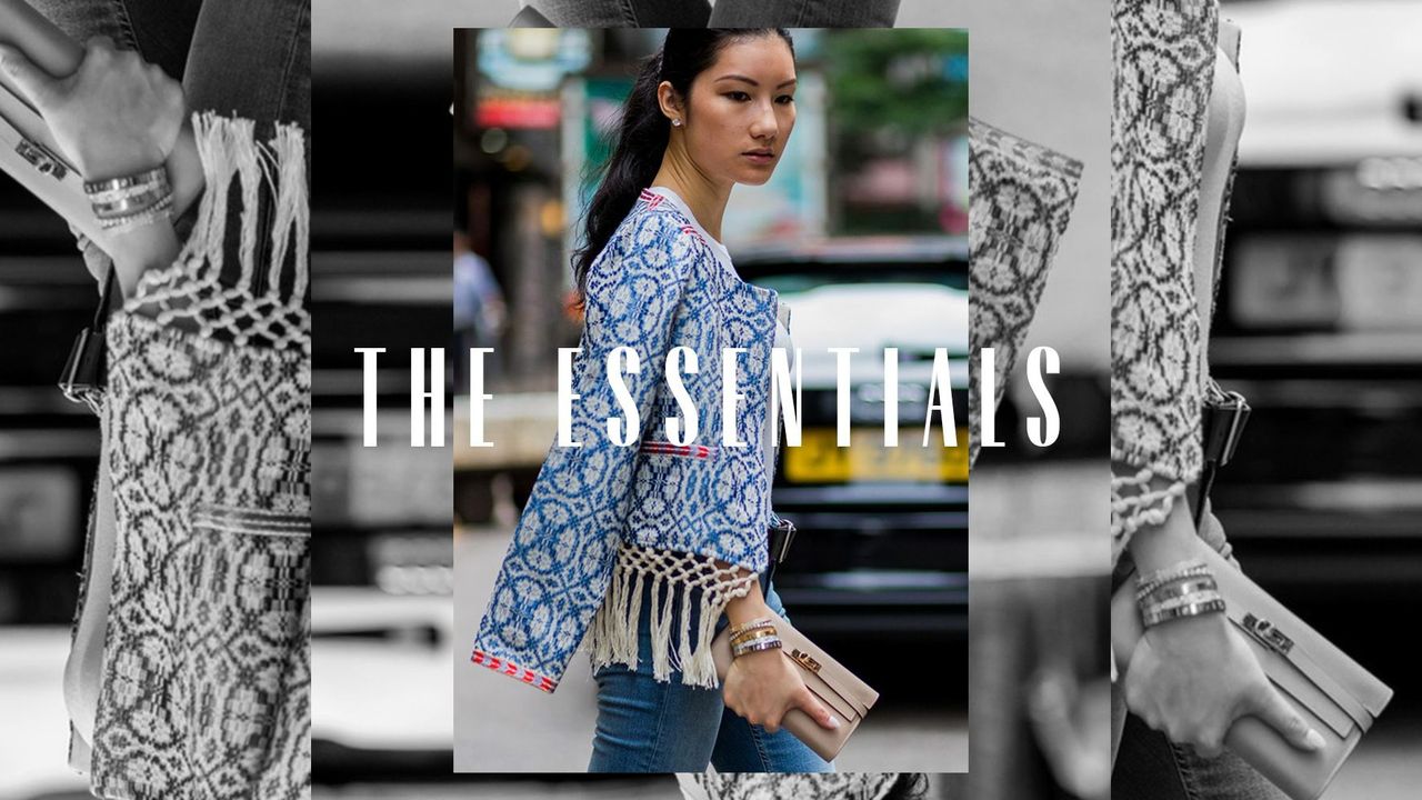 A woman walks through the street carrying a purse. Text overlay reads, &quot;The Essentials.&quot;