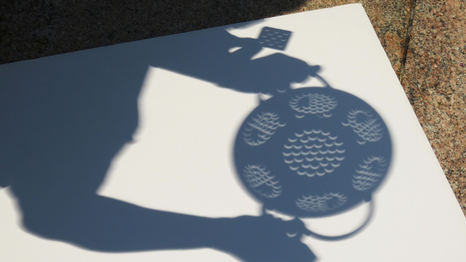 tiny half-moon shapes can be seen in the holes in the shadow of a colander held by two hands