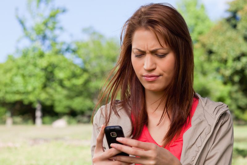 A woman looks confused as she reads a text message on her phone.