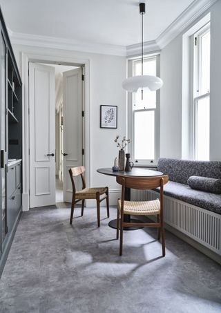 white dining room with grey floor, grey upholster window seat, retro chairs and table, white pendant