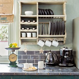 Section of kitchen worktop in a green kitchen with coffee machine on worksurface and wall shelves above with hanging mugs