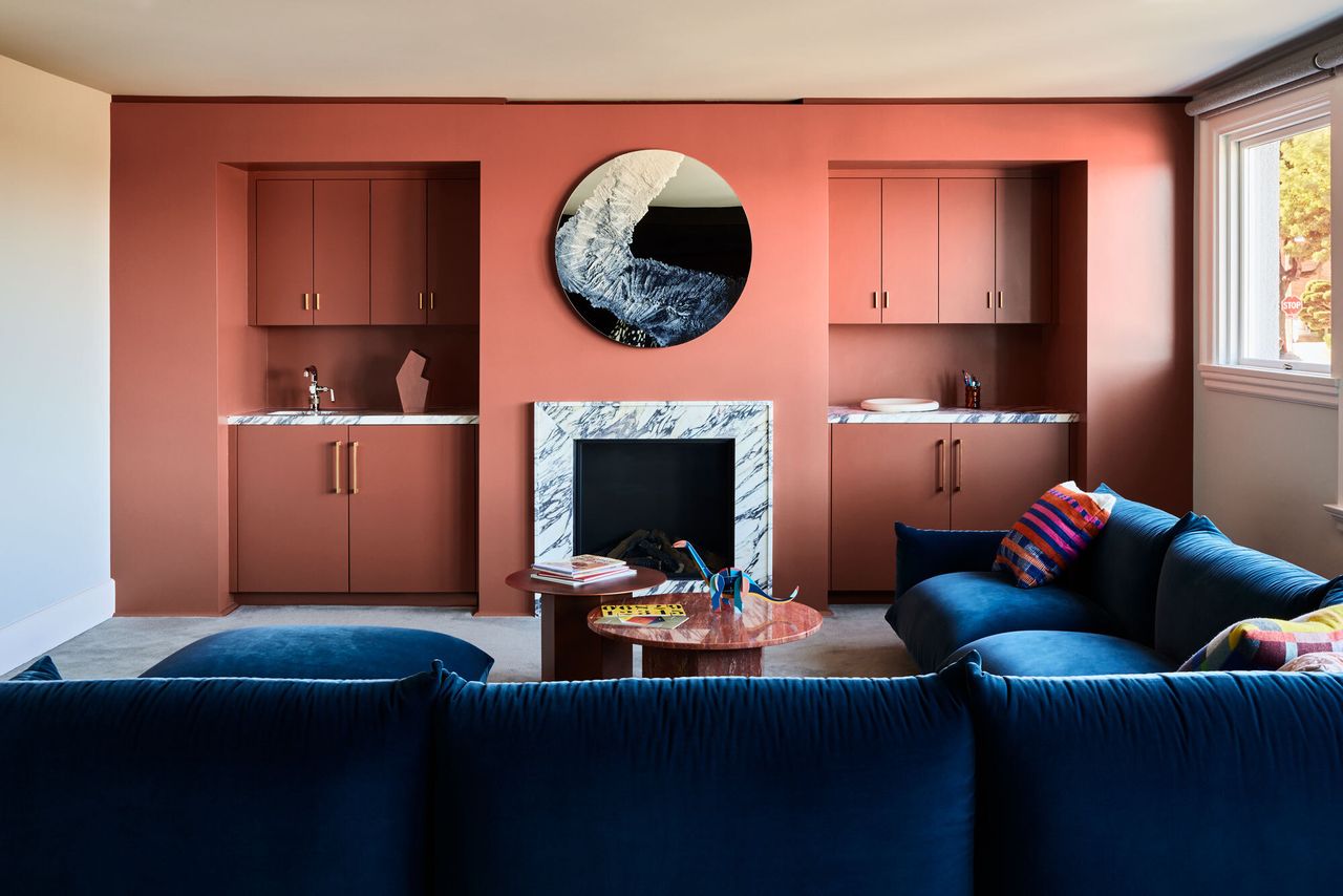 The family room in a San Francisco renovation featuring a large mirror above the fireplace and accent blue sofa and pink wall