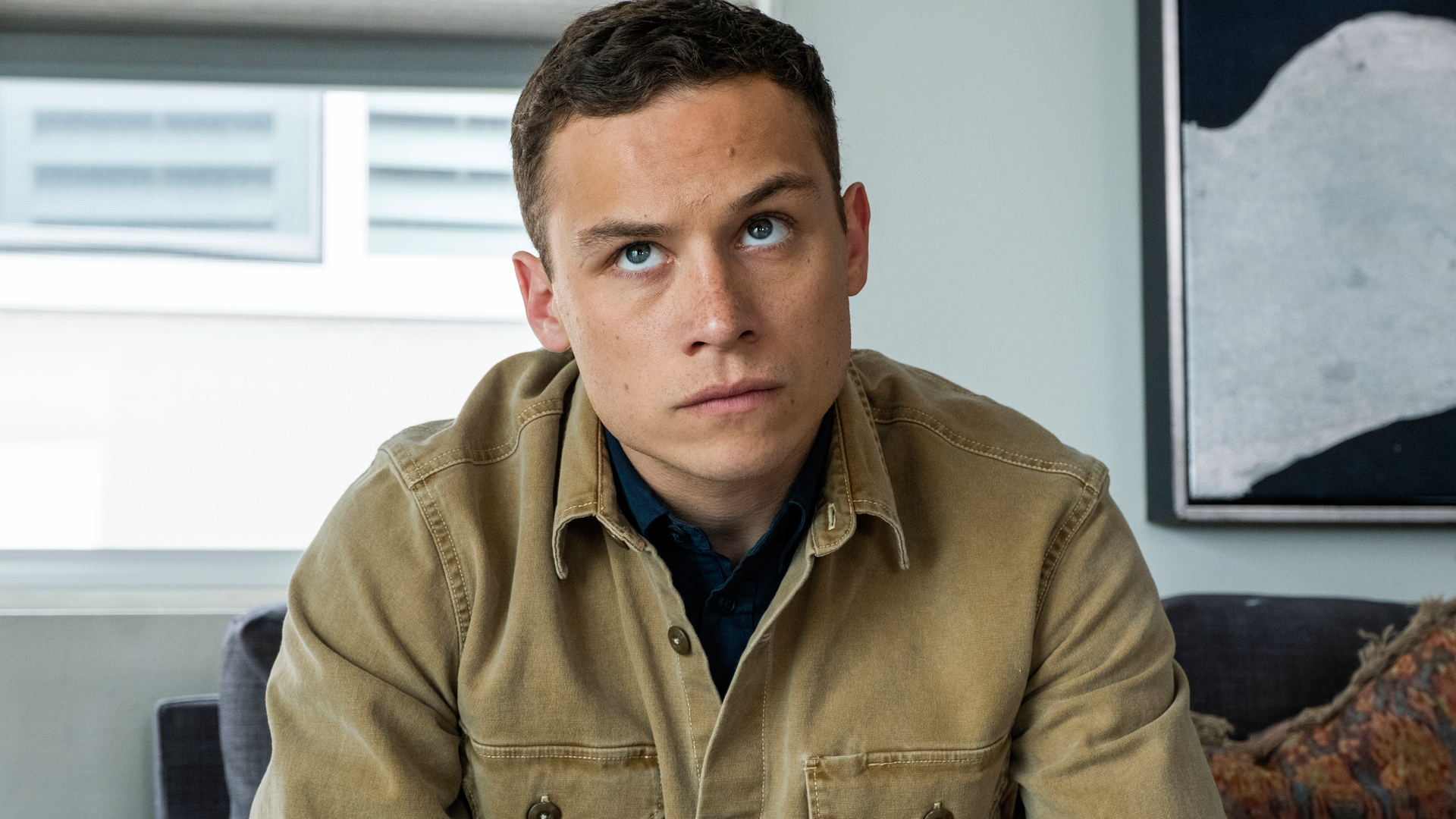 "J" (Finn Cole) in a beige work jacket sitting on a sofa in a scene from "Animal Kingdom" season 5