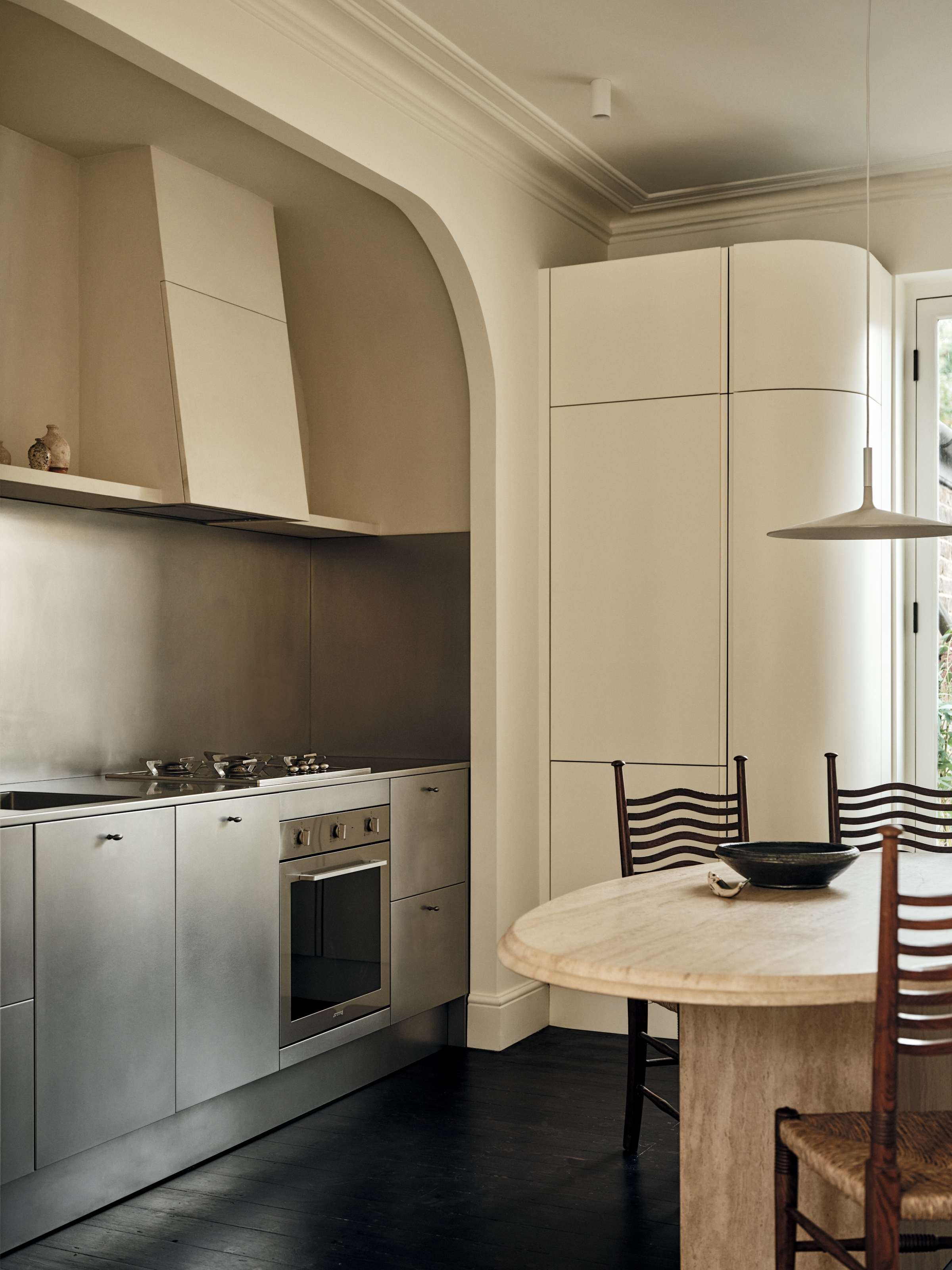 Stainless steel kitchen set into warm off-white joinery with a travertine dining table
