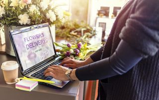 A laptop is open with a flower delivery site displayed. A person is looking at the laptop.