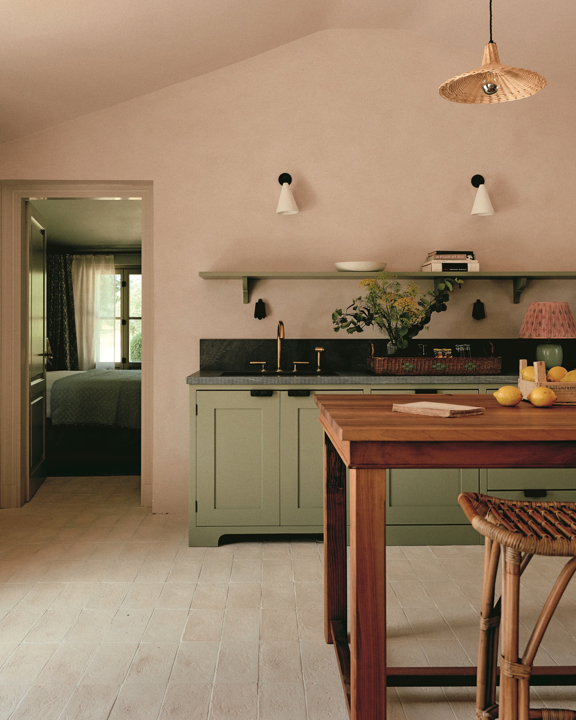 kitchen with matcha green cabinetry and plaster pink walls with freestanding timber island bench and rattan stool