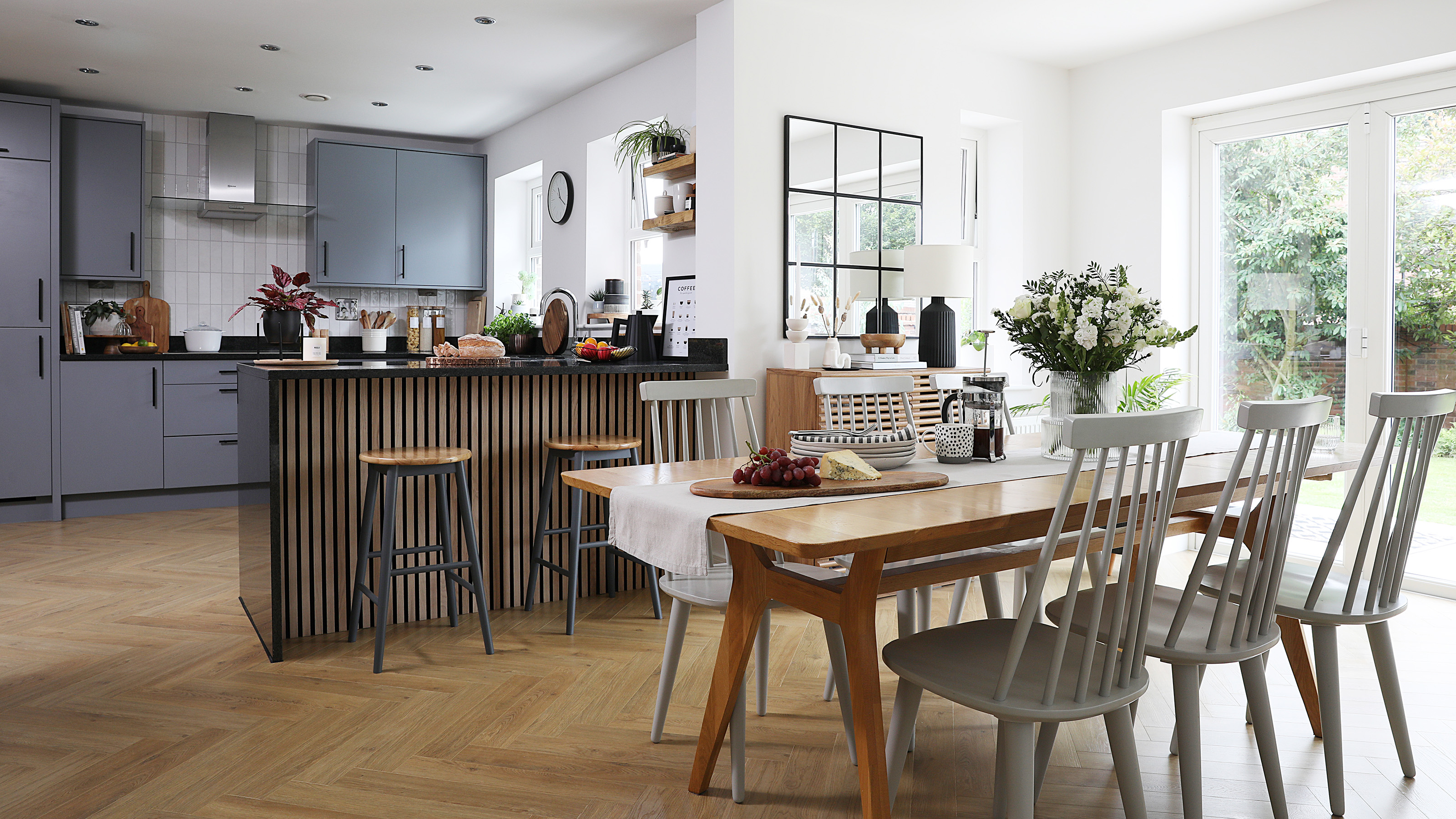 open plan kitchen diner with grey cabinets and island with wooden slat front dining table with grey farmhouse chairs and herringbone wood flooring