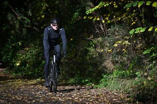 Male cyclist riding a Ribble Allroad Ti road bike on a leaf-covered lane wearing black Castelli Soprasso RoS Wind Bibtight and black Espresso Air jacket