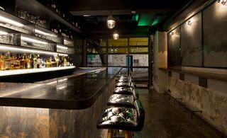 Fatty Crab, Hong Kong, China. A bar area with a long wooden counter, leather topped high chairs and glass and liquor wall shelving.