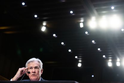A pensive Jerome Powell sits under a row of intense lights