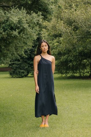 A model standing in grass wearing a one-shoulder black dress