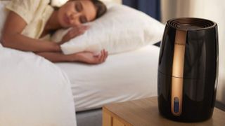 En kvinna sover i sin säng med en svart Philips luftfuktare på nattduksbordet bredvid.