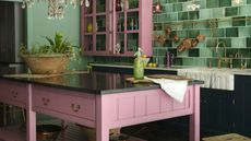 A modern traditional kitchen with green tiled wall decor, pink island furniture and statement lighting fixtures