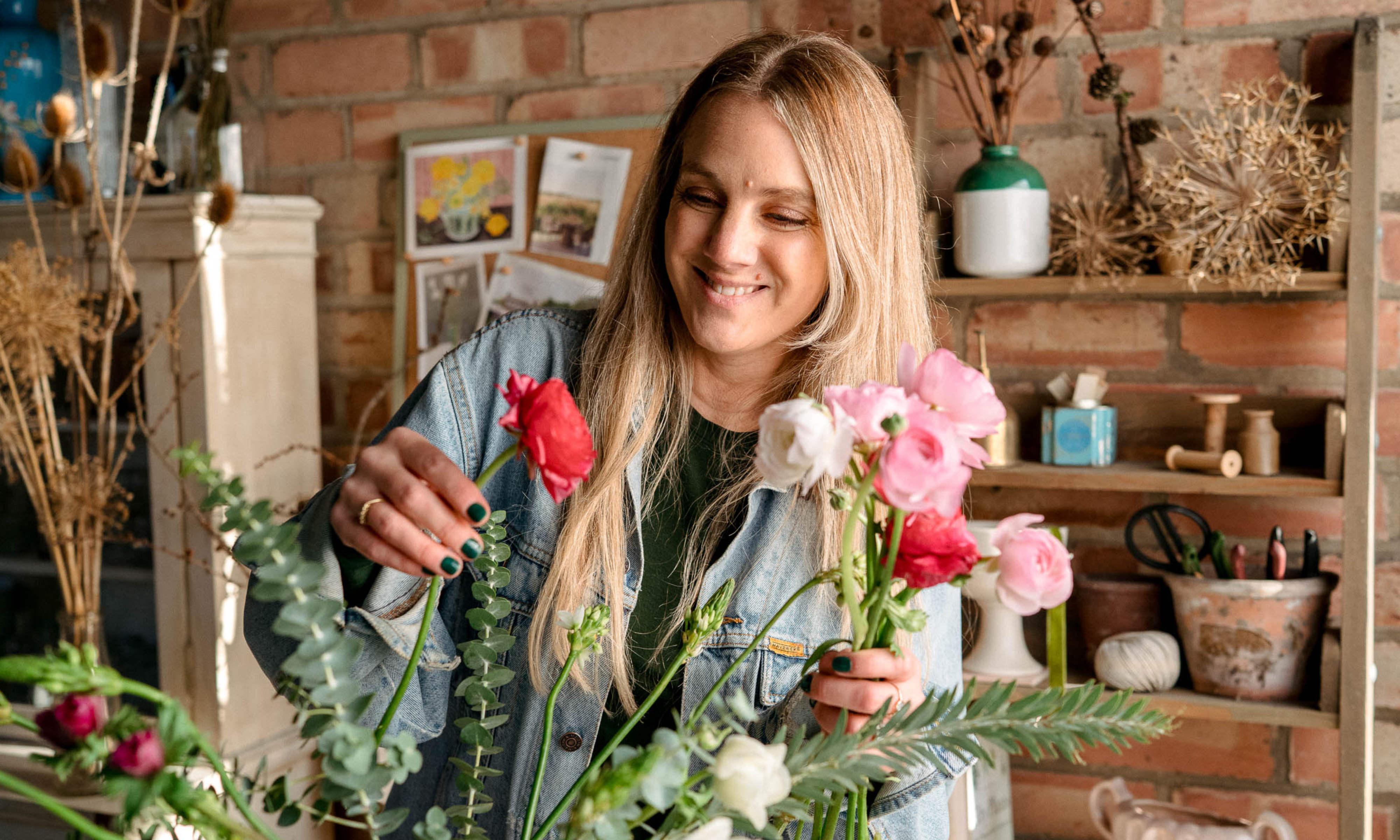 Woman placing pink ranunculus flower into an arrangement