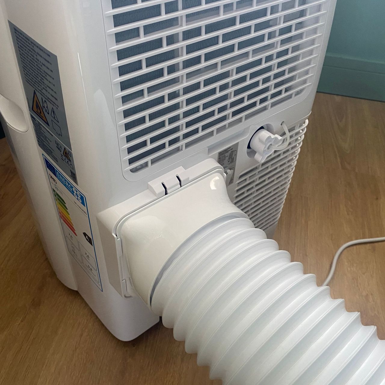 Exhaust hose attached to the back of the Dreo 318s portable air conditioner in a green room with wood-look floors
