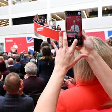 MANCHESTER, ENGLAND - JUNE 13: A woman films on a mobile phone as Labour Party leader Sir Keir Starmer speaks during the launch of Labour's general election manifesto on June 13, 2024 in Manchester, United Kingdom. Labour is consistently leading the polls by over 20 points, according to the latest YouGov data. (Photo by Anthony Devlin/Getty Images)