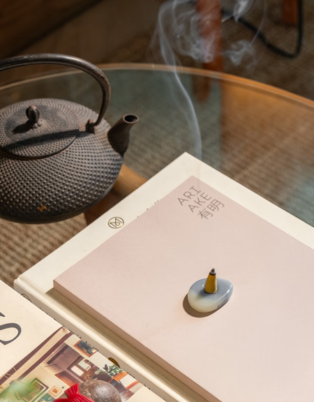 A yellow incense cone on a seaglass holder on a glass coffee table with books and a tea pot