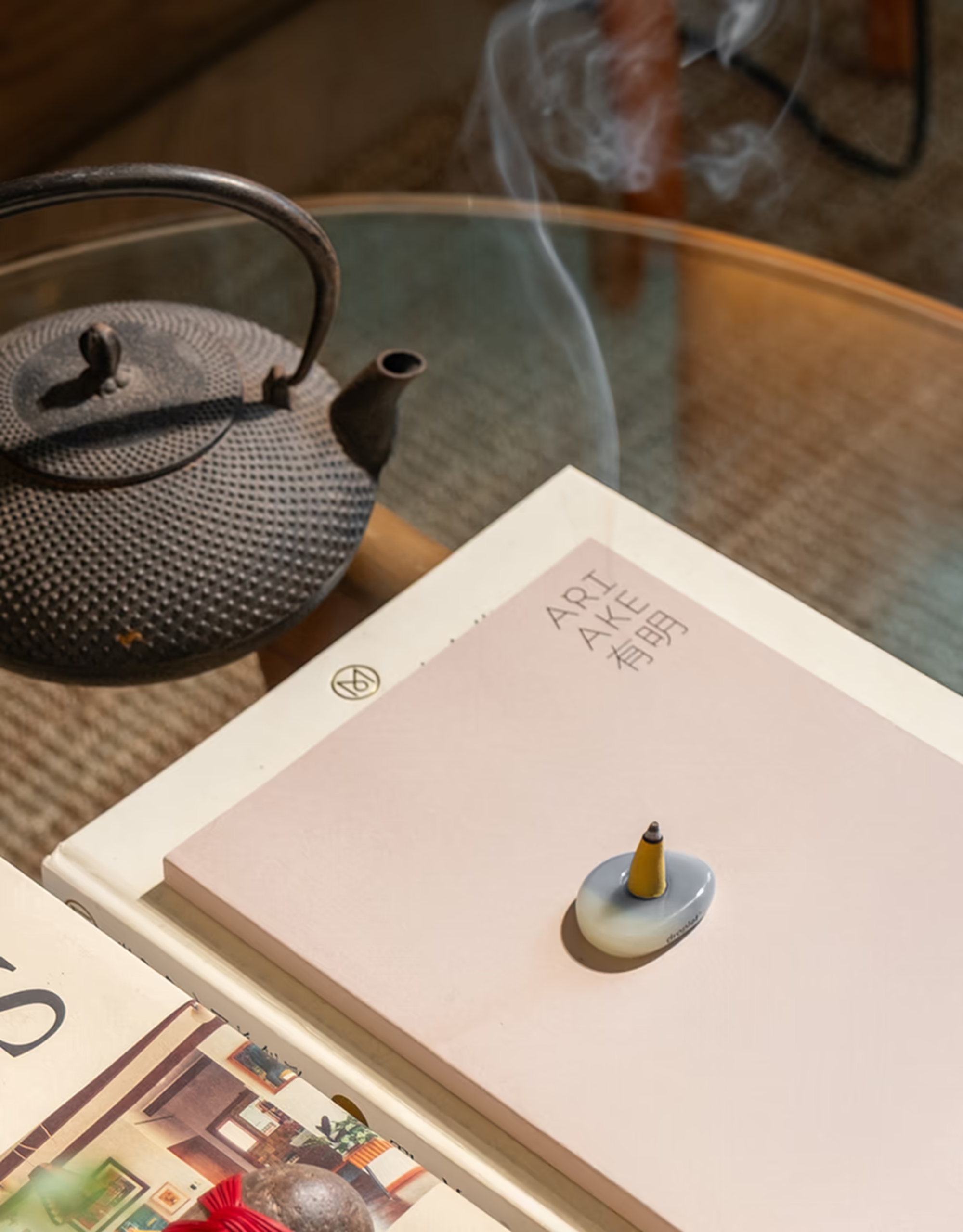 A yellow incense cone on a seaglass holder on a glass coffee table with books and a tea pot