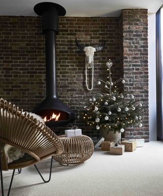 A rustic Christmas-themed living room with modern fireplace, cream linen wool carpet, small decorated Christmas tree and rattan chair and footstool