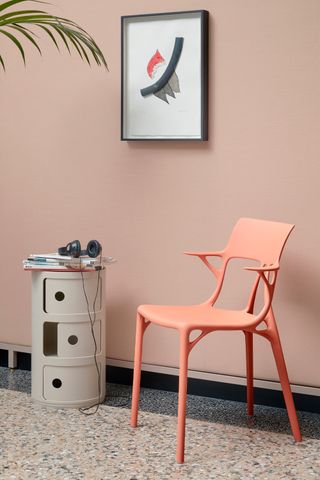 Philippe Starck’s ‘A.I.’ chair in recycled plastic. A pink plastic chair next to a round chest of drawers in front of a pink wall with a wall painting on it.