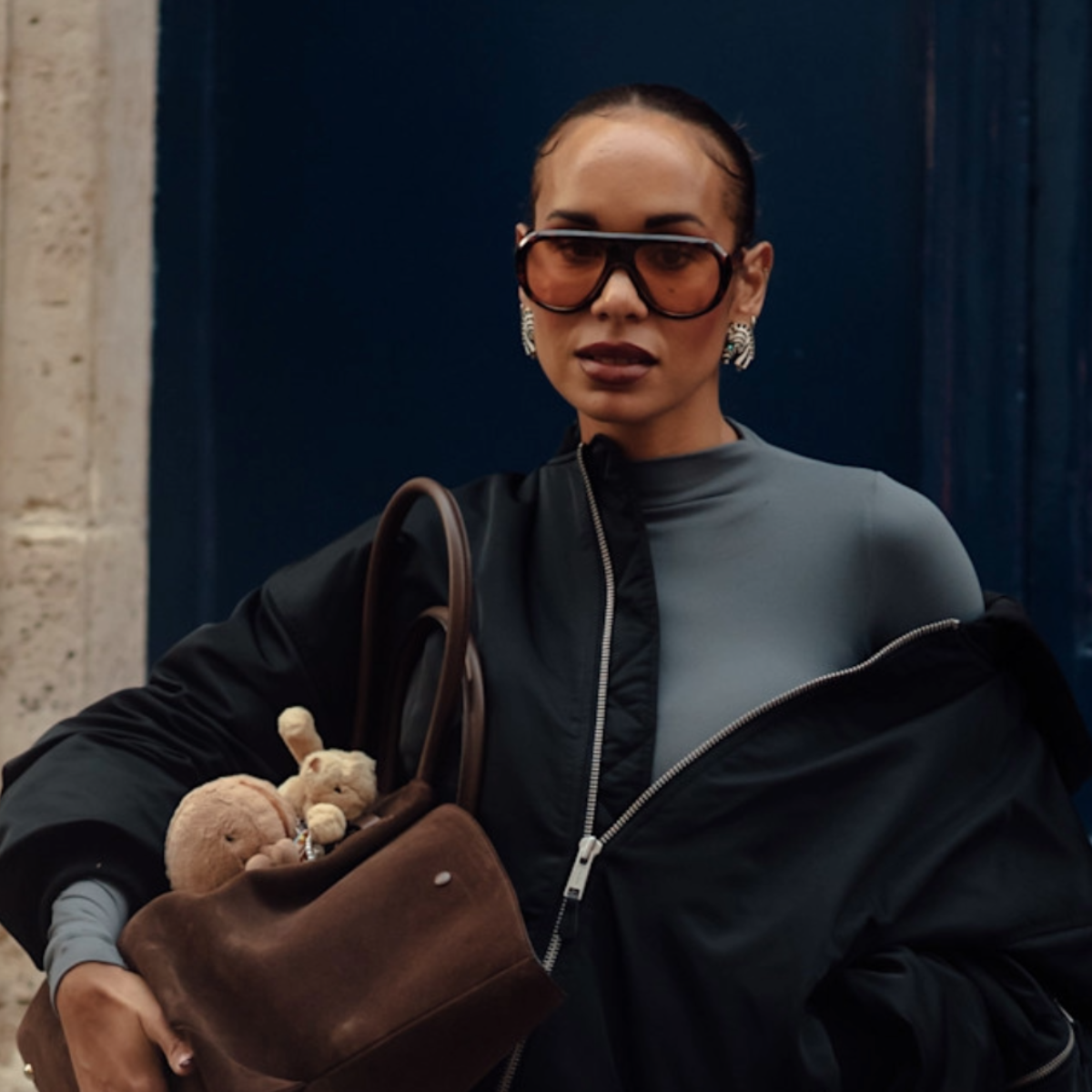 woman wearing sunglasses and a jacket with a gray turtleneck dress.