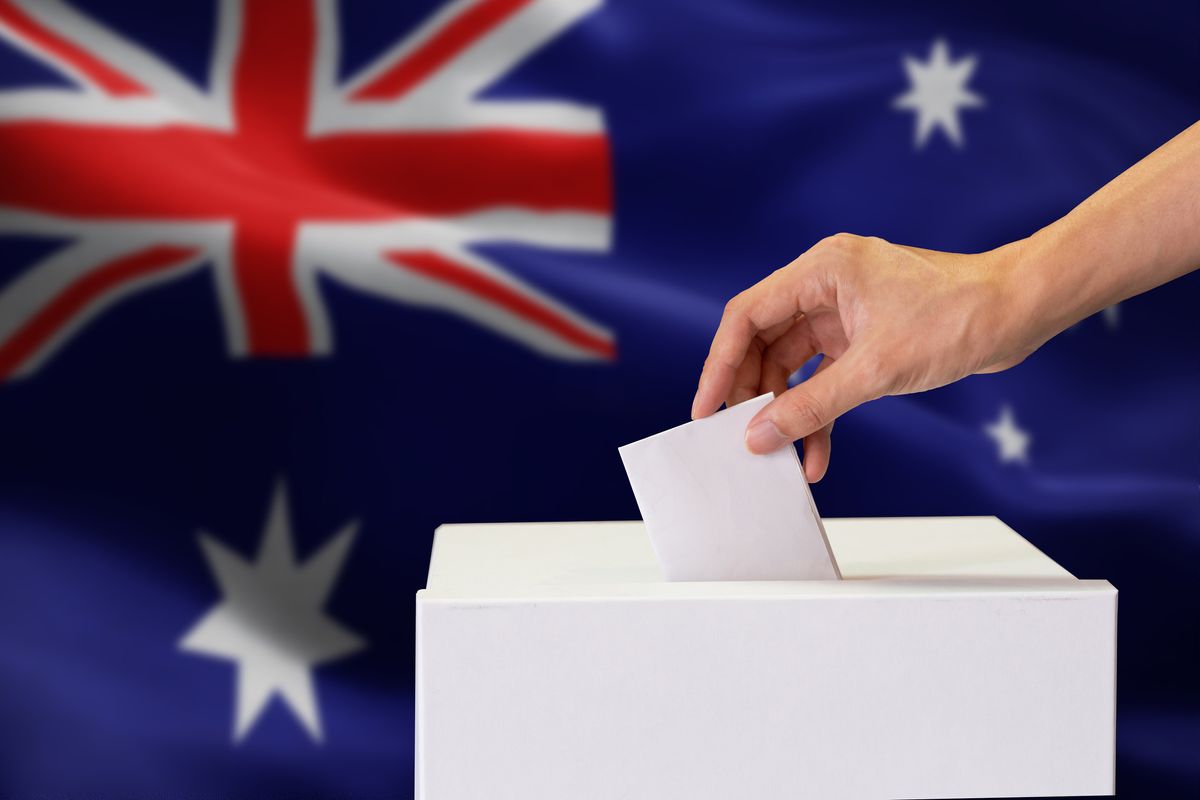 A hand placing a ballot paper into a voting box with the Australia flag in the background