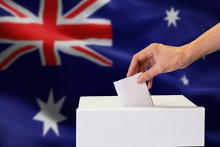 A hand placing a ballot paper into a voting box with the Australia flag in the background