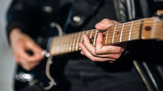 Closeup of a man's hands playing a Fender Telecaster-style guitar.