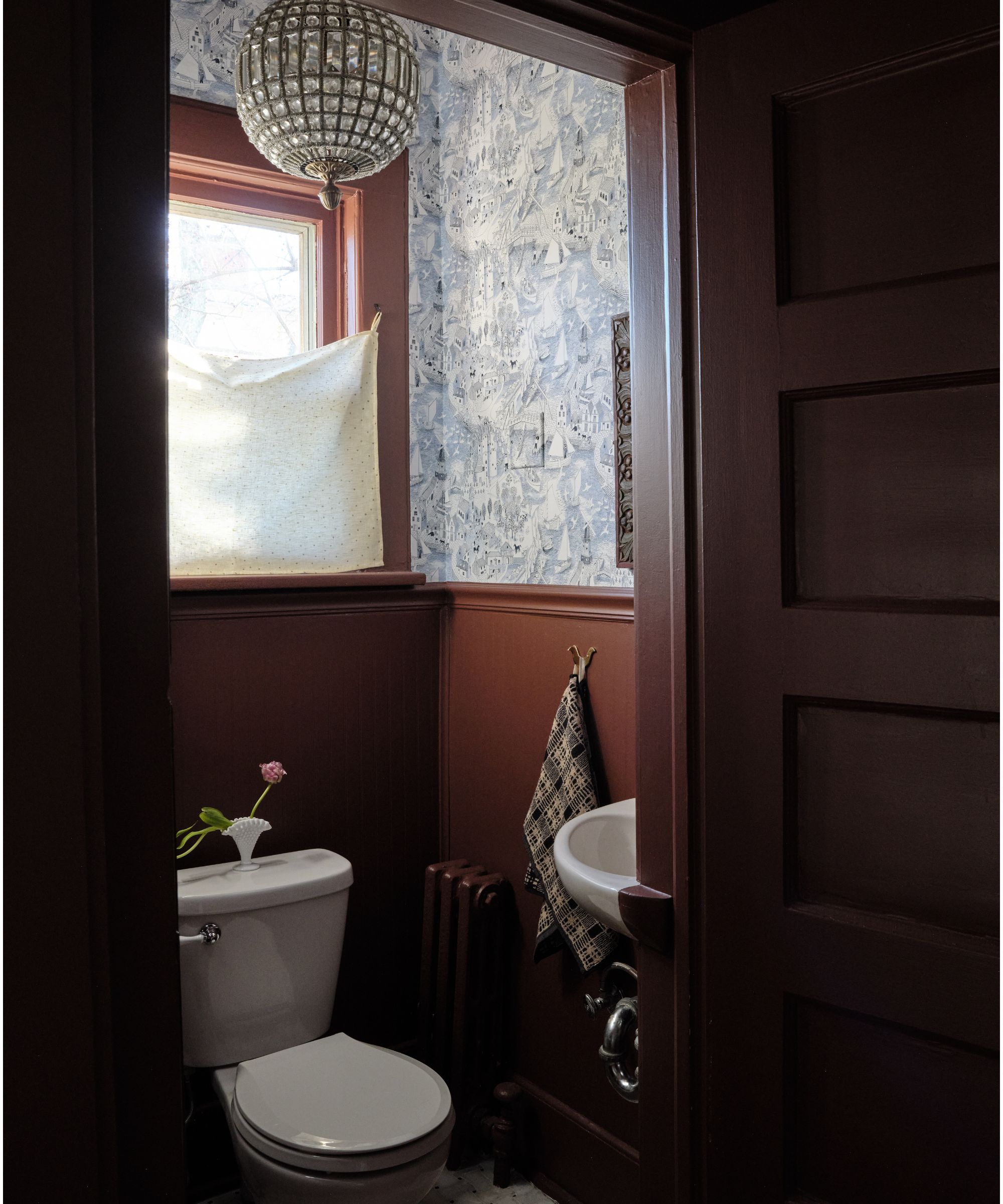 dark moody red painted powder room with blue printed wallpaper, a slung cafe curtain and vintage globe light